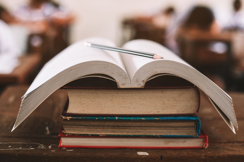 Open old book and pencil stand on the desk with students taking