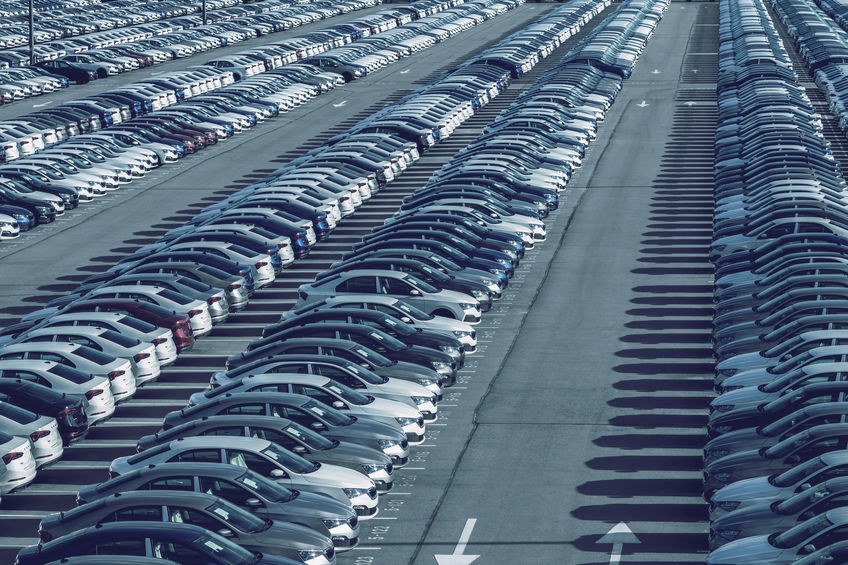 Rows of a new cars parked in a distribution center on a car factory on a sunny day. Top view to the parking in the open air.
