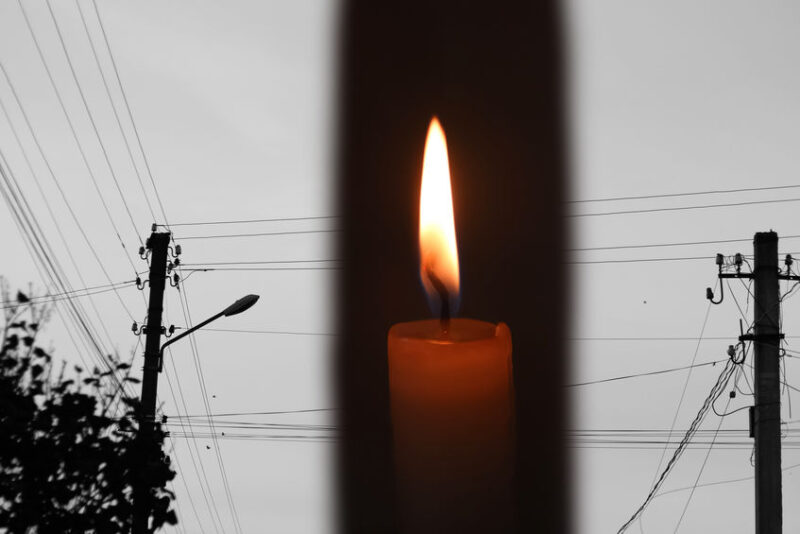 Blackout, power grid overloaded. Blackout concept. Earth hour. Burning flame candle and power lines on background. Energy crisis. Dark night. Candle flame