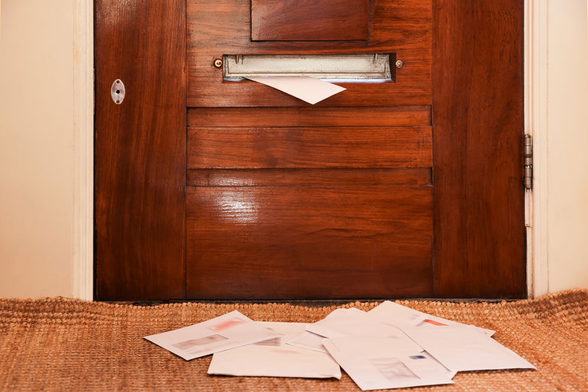 Wooden door with mail slot and many envelopes indoors