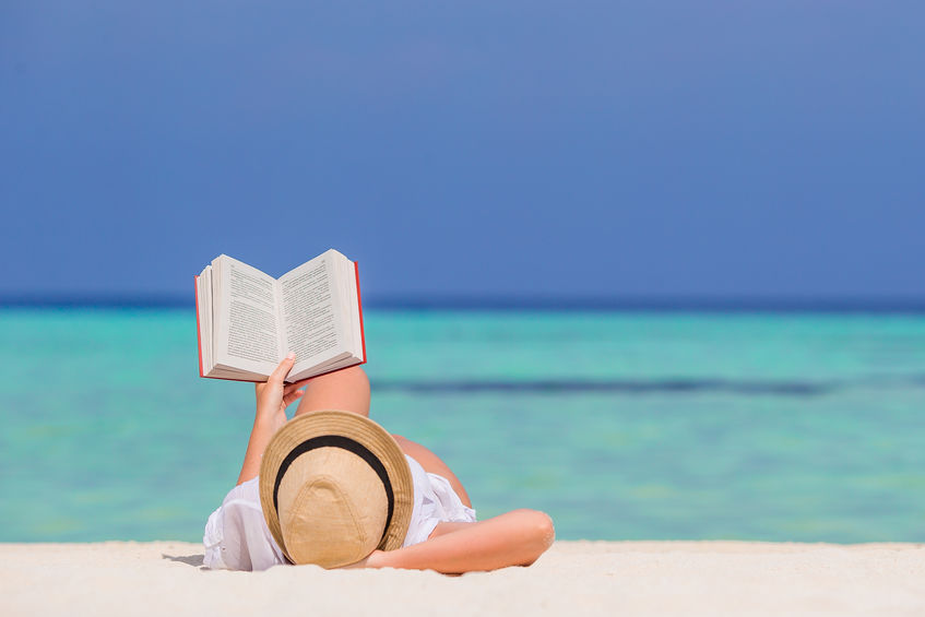 Portrait of a young woman relaxing on the beach, reading a book