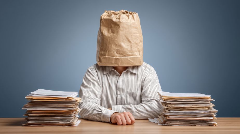 Person with Brown Paper Bag Sitting at Desk Surrounded by Stacks of Papers Quirky Concept Illustrating Office Stress, Workload, and Identity Crisis