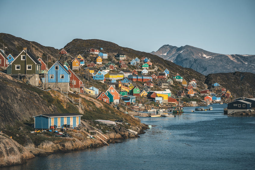 Colorful houses dot the hillsides of the fishing town of Kangaamiut, West Greenland. Icebergs from Kangia glacier in Greenland swimming with blue sky and clouds. Symbol of global warming.